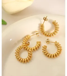 Macro detail of golden spiral texture C-shaped hoop earrings on a ceramic tray