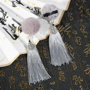 Dettaglio di fermagli per capelli con nappe grigie, pompon e elementi in metallo argento