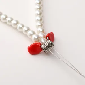 Detalle macro de perlas blancas y cuenta de corazón rojo con conectores espirales plata