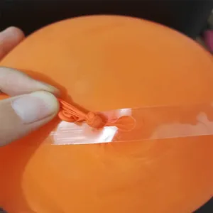 Hand inserting orange balloon into transparent PVC hole strip for party arch decoration