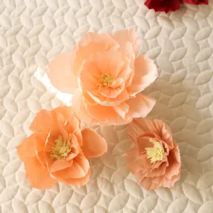 Three sizes of handmade crepe paper flowers in soft pink and orange tones for wedding decor