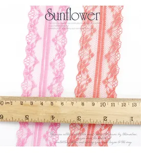 Detail of 4cm polyester lace ribbon in pink and peach colors with wavy edges and ruler