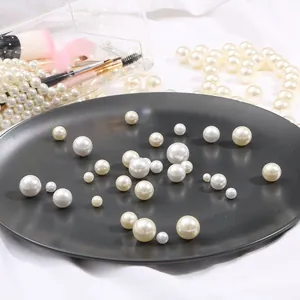 Mixed sizes of white round faux pearls for DIY crafts on a textured black tray background