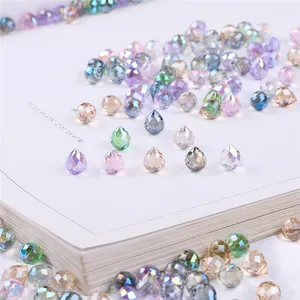 Faceted teardrop glass crystal beads in colorful iridescent shades on a book