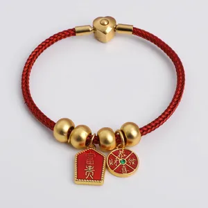 Detail of red braided bracelet with gold lucky charms and Fu-Gui enamel pendants
