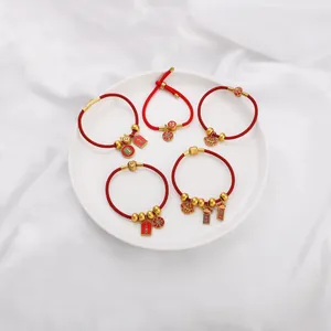Detail of red braided bracelets with gold-plated lucky charms in a white dish