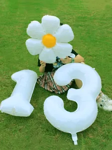Detalle de globos blancos número 13 de 32 pulgadas y margarita sobre hierba verde