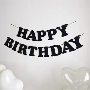 Dettaglio dello striscione Happy Birthday in feltro nero appeso su una parete bianca