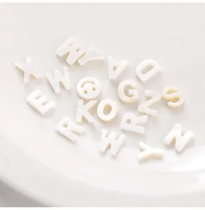 Macro detail of white natural shell alphabet beads and smiley face charm for DIY jewelry