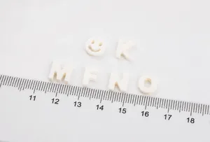 Detail of white shell alphabet beads with smiling face icon next to a measurement ruler