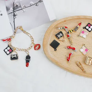 Bracciale dorato con ciondoli in smalto a forma di rossetto su vassoio di legno