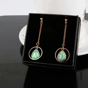 Détail de boucles d'oreilles opale en forme de goutte d'eau avec bords dorés et chaînes