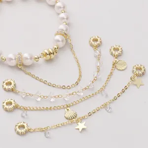 Dettaglio di ciondoli a stella marina dorati e perle bianche su un bracciale a strati