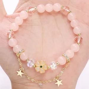 Bracciale di perle rosa con ciondolo a fiore giallo e stelle dorate sulla mano