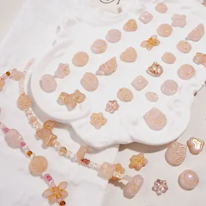 Pink translucent butterfly and heart glass beads with gold patterns in a white tray