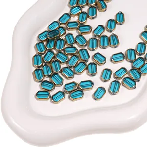 Macro detail of teal faceted glass beads with gold metal edges on a ceramic tray