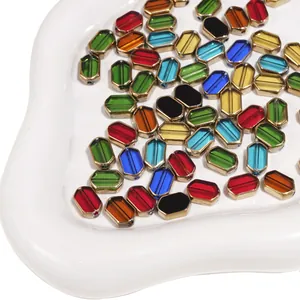 Close-up of colorful rectangle glass beads with gold trim in a white ceramic tray