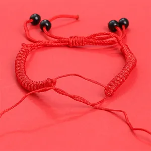 Détail macro du bracelet en cordon rouge tressé avec perles noires et nœud plat ajustable
