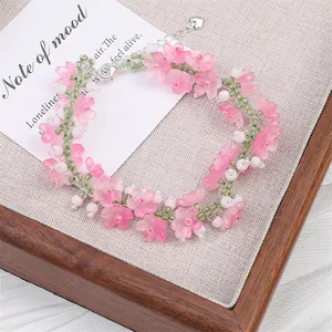 Detailed shot of handmade bracelet with pink glass flowers and green beads on a wooden tray