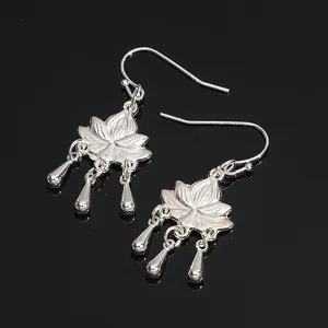 Silver lotus dangle earrings with teardrop pendants on a black reflective surface