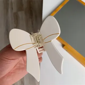 Close-up of a white acetate bow hair claw clip with elegant gold wire detailing