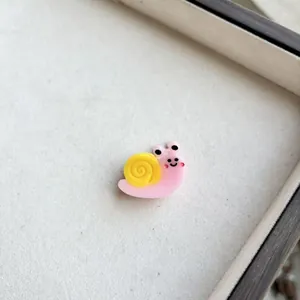 Macro detail of mini resin snail hair clip with cute pink face and yellow shell design