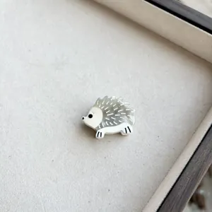 Macro shot of cute resin hedgehog brooch with translucent spines on beige texture