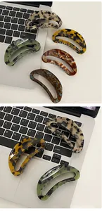 Close-up of five acetate hair claws with leopard and marble patterns on a laptop background