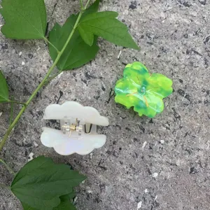 Mini floral acetate hair claws in neon green and pearlescent white on stone surface
