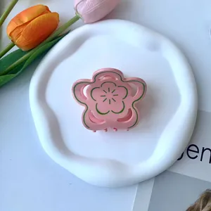 Dettaglio molletta per capelli a fiore in acetato rosa e verde su piatto bianco