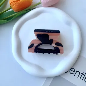 Dettaglio della molletta per capelli in acetato rosa con cuori neri su vassoio ceramico
