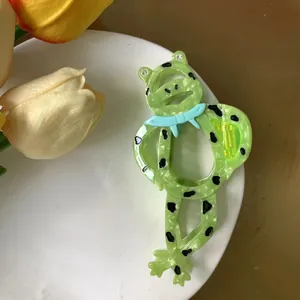Cute green frog hair claw clip with blue bowtie and rhinestones on a white plate