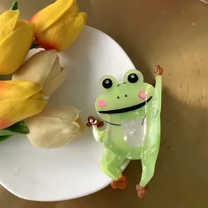 Cute green frog hair claw clip made of acetate with big eyes on white porcelain plate