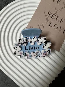 Dettaglio del fermaglio per capelli in acetato blu con bordo ondulato e logo Likio su marmo