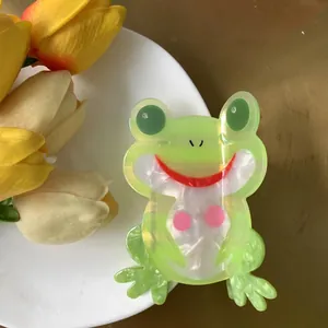 Detail of a green cartoon frog hair claw clip made of pearlescent acetate on a white plate