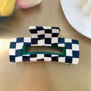 Elegant checkered rectangle hair claw clip with green interior on a gold surface