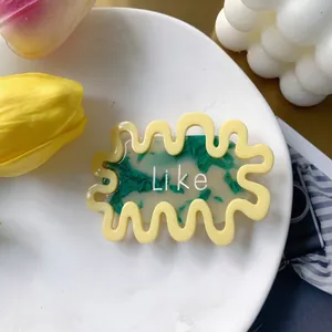 Detail of yellow wavy hair clip with green marble pattern and Like text cutout