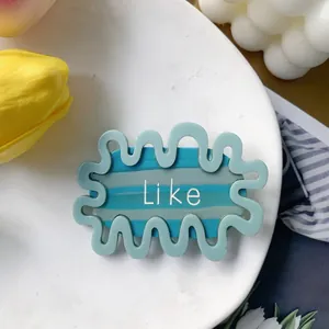 Macro view of blue wave-shaped acetate hair clip with Like text and decorative items