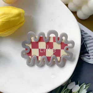 Detail of wavy acetate hair clip featuring red checkerboard pattern and Like text