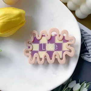 Close-up of wavy acetate hair clip with pink frame, checkerboard pattern and Like text