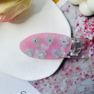 Gros plan d'une pince à cheveux en acétate rose avec fleurs 3D blanches et strass brillants