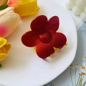 Close-up of a glossy red flower hair claw clip with contrasting yellow teeth on white tray
