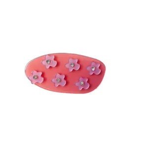 Pince à cheveux rose en acétate avec fleurs et strass sur un fond blanc épuré