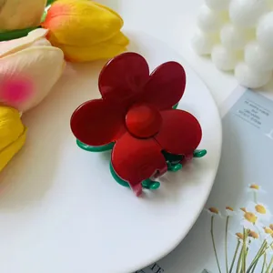 Detailed close-up of a red flower hair claw clip with green teeth on a white plate