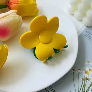 Detail shot of a yellow five-petal flower hair claw clip with green teeth on a white tray