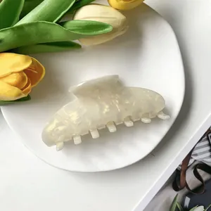 Vue macro d'une pince à cheveux crème en acétate avec texture marbrée nacrée sur plat blanc