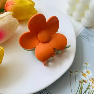Detail of orange flower hair claw clip with green teeth on a decorative white plate