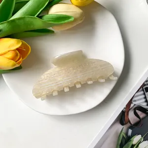 Détail d'une pince à cheveux en acétate blanc crème avec texture nacrée sur un plateau