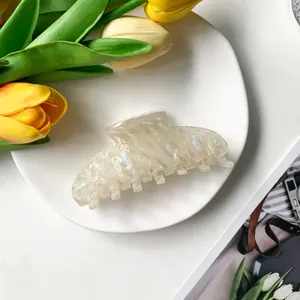 Détail d'une grande pince à cheveux en acétate nacré disposée sur une assiette en céramique