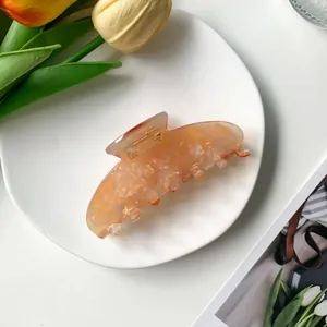 Gros plan d'une pince à cheveux de 9cm en acétate pêche avec texture nacrée sur assiette